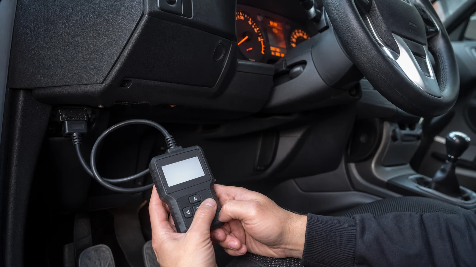 Driver using a handheld OBD2 code reader under a UK car dashboard